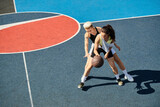 Two athletic women stand on a basketball court, celebrating their friendship and love for the game on a sunny summer day.