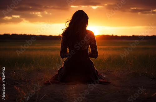 Prayer concept. Silhouette of a pretty young teen woman in a praying pose. Set against a vibrant sunset sunrise sky. Clasped hands. Also related to renewal, connection, journey, gratitude, encounter