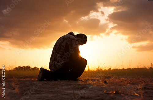 Prayer concept. Silhouette of a man on his knees in a praying pose. Set against a vibrant sunset sunrise sky. Clasped hands. Also related to discernment, graceful, gracious, spirit-filled, repentance photo