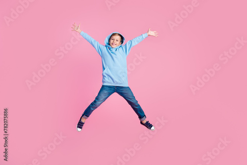 Full size photo of small overjoyed boy jumping raise hands make star symbol empty space isolated on pink color background