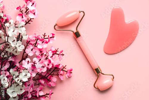 Closeup of pink jade roller, jade gua sha massager stone and almond blossoms. Skin care products concept photo