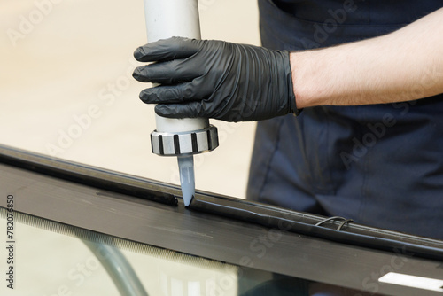 Automobile glazier adding glue on windscreen or windshield of a car in auto service station garage before installation