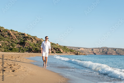Handsome happy man in white shirt walking on the beach. Summer vacations concept.