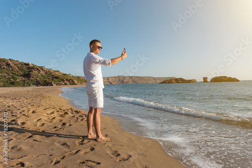 Handsome happy man in white shirt taking selfie on the beach. Summer vacations concept.