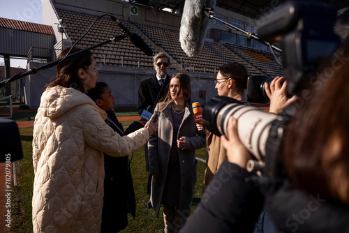 Two organization representative answer press questions and give interview outside on a soccer stadium. Interview of successful SEO at press conference for TV news. Journalists crowd on press campaign. © Framestock