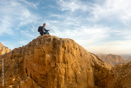 Man hiker sitting on top of a rocky mountain looking at the view © Rob Wilkinson