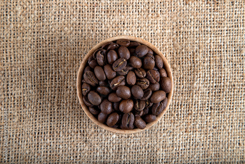 A bowl full of roasted coffee beans on burlap sack ,top view
