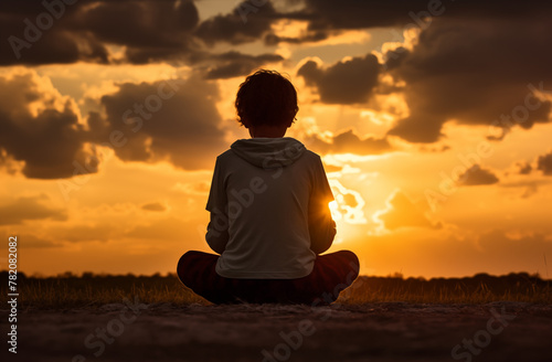 Prayer concept. Silhouette of a black boy child in a praying pose. Set against a vibrant sunset sunrise sky. Clasped hands. Also related to reverent, inner, uplifting, radiance, sacred