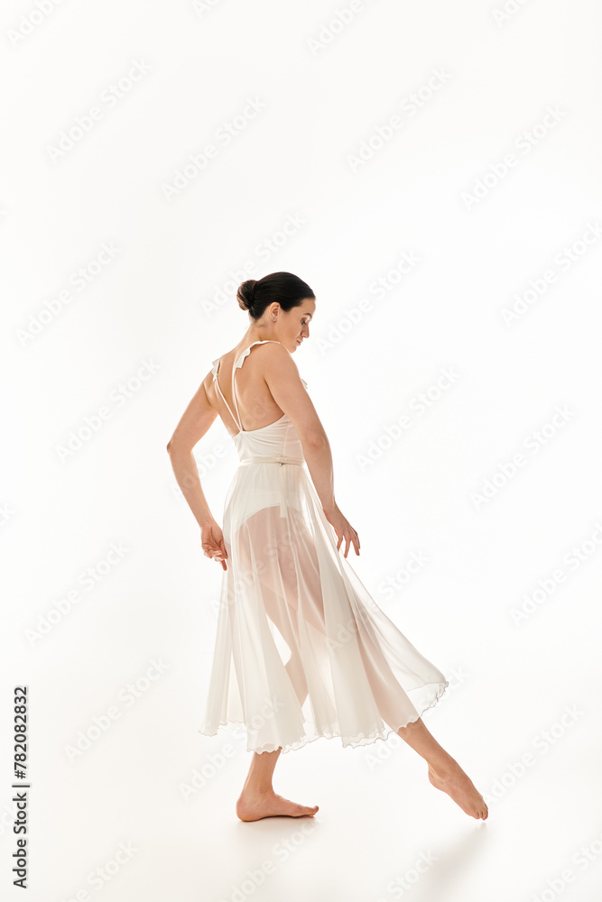 A young woman in a flowing white dress gracefully dances in a studio setting against a white background. A young woman in a flowing white dress gracefully dances in a studio setting against a white background.