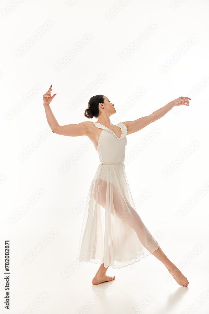 A young woman in a long, flowing white dress gracefully dances in a studio setting against a white background.