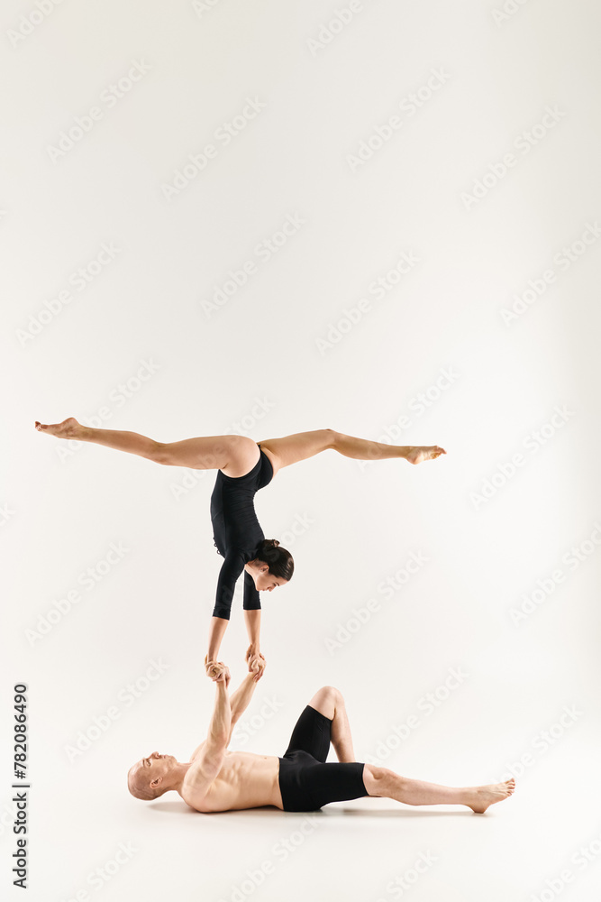 Shirtless young man and dancing woman defy gravity in a synchronized handstand pose against a white studio backdrop.