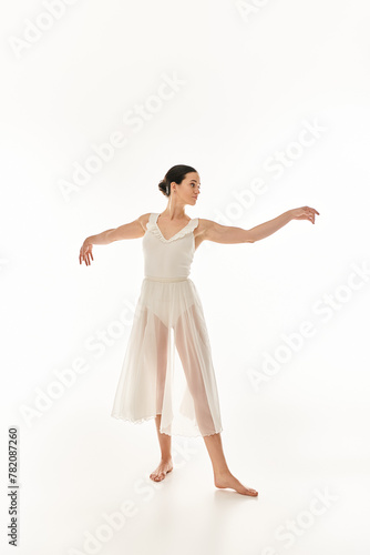 A young woman in a long white dress stands with her arms outstretched in a graceful dance pose against a white studio backdrop.