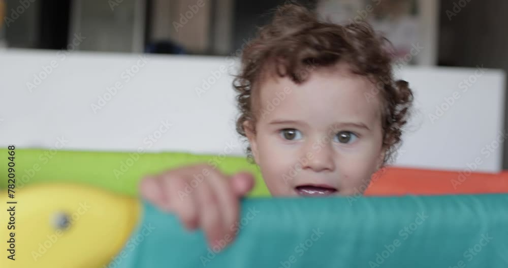 Toddler peeking over bright orange playpen indoors during playtime Toddler peeking over bright orange playpen indoors during playtime