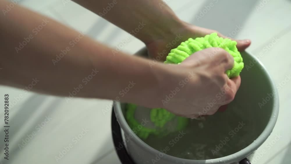 Cleaning the house, a man is about to wash the floor and wets a rag for washing the floor in a bucket before putting it on the mop. Cleaning the house, a man is about to wash the floor and wets a rag for washing the floor in a bucket before putting it on the mop.