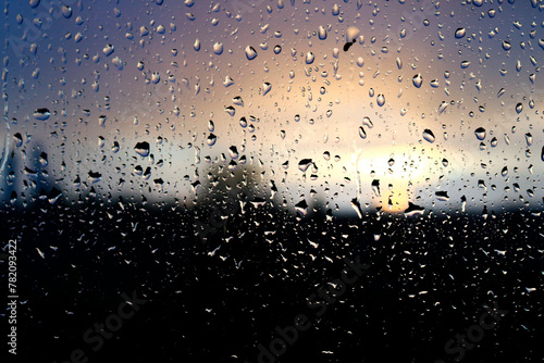 Stunning photoshoot of raindrops on a window with background of sunset in the sky. Wallpaper image with water drops and blurred sky and clouds on the background