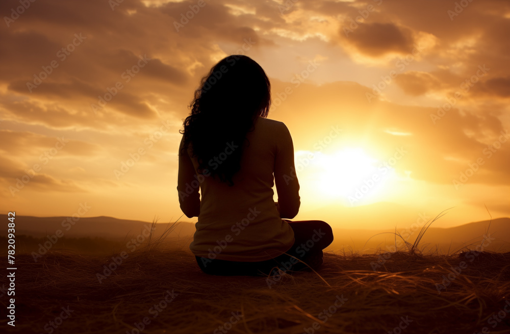 Prayer concept. Silhouette of a pretty teen woman in a praying pose. Set against a vibrant sunset sunrise sky. Clasped hands. Also related to serenity, compassion, mystery, presence, renewal