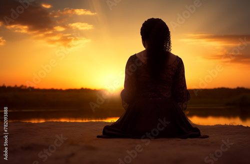 Prayer concept. Silhouette of a pretty African american woman in praying pose. Set against a vibrant sunset sunrise sky. Clasped hands. Also related to vicarious, word of god, zion, reverence, divine photo