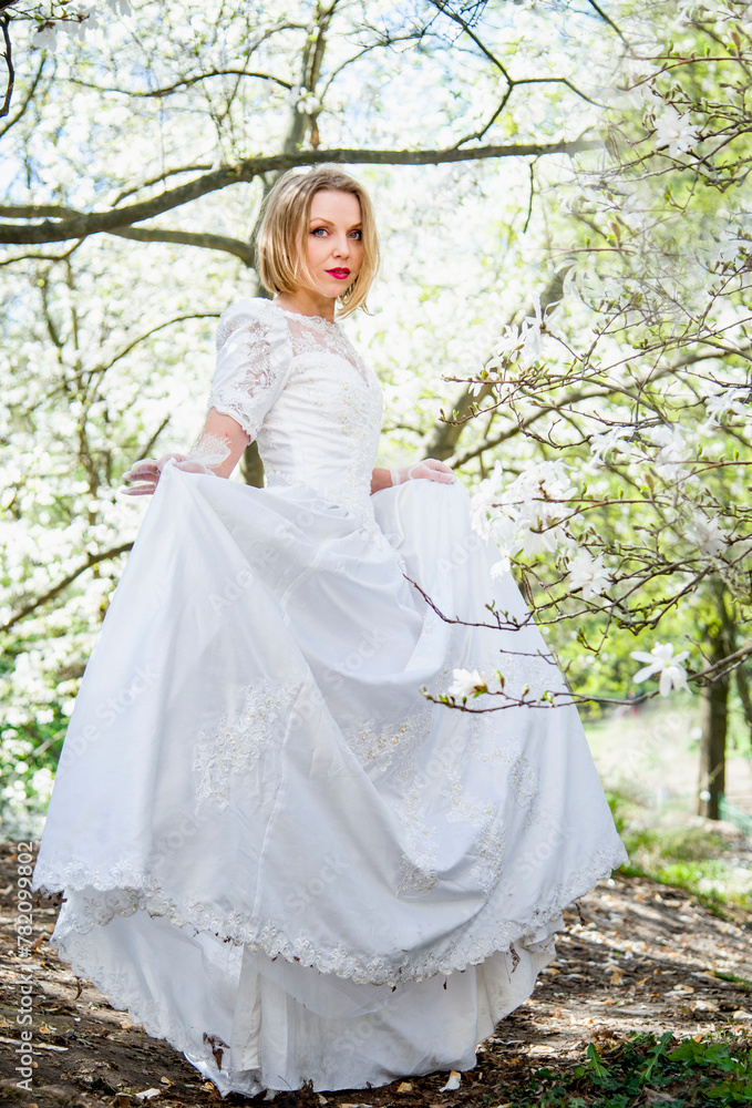 beautiful blonde smiling romantic bride in a white dress walking in blossoming magnolia garden on sunny spring day beautiful blonde smiling romantic bride in a white dress walking in blossoming magnolia garden on sunny spring day