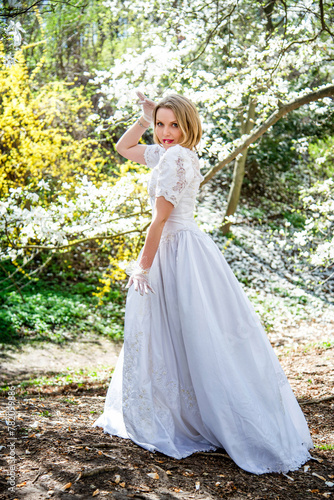beautiful blonde smiling romantic bride in a white dress walking in blossoming magnolia garden on sunny spring day