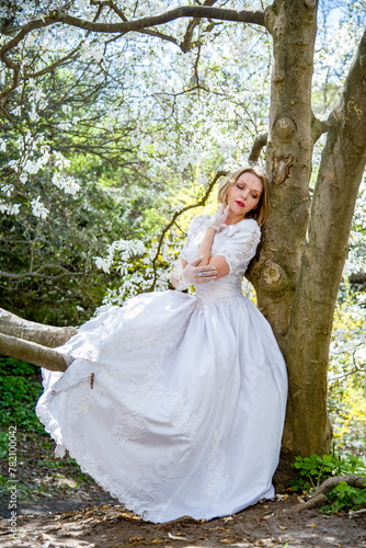 beautiful blonde smiling romantic bride in a white dress walking in blossoming magnolia garden on sunny spring day