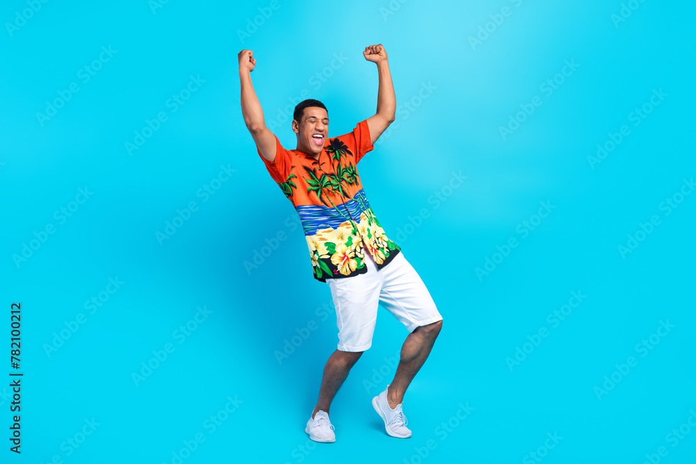 Full length photo of carefree lucky guy dressed print shirt having fun rising fists isolated blue color background Full length photo of carefree lucky guy dressed print shirt having fun rising fists isolated blue color background