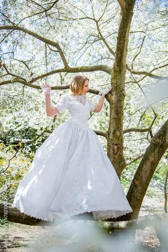 beautiful blonde smiling romantic bride in a white dress walking in blossoming magnolia garden on sunny spring day