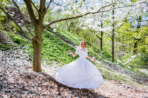 beautiful blonde smiling romantic bride in a white dress walking in blossoming magnolia garden on sunny spring day