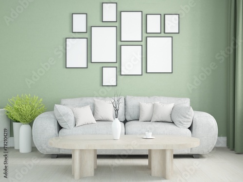 ściana zielonego pokoju salonu z wiszącymi ramkami na obrazy szarą sofą z poduszkami i stolikiem kawowym