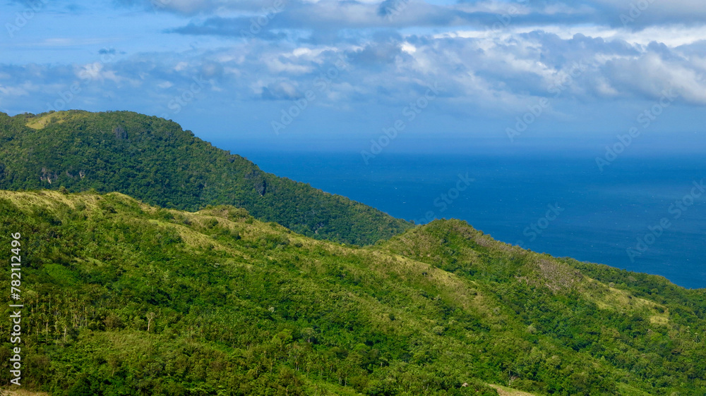 Aerial view of the mountain range of a tropical island. Mountains and hills of a tropical island covered with jungle against the backdrop of the blue sea.