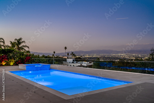 Empty swimming pool with city lights in the distance under a clear blue sky © Wirestock