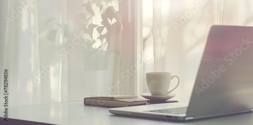laptop on a white desk, a coffee cup and book beside it, white background