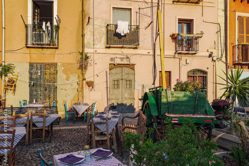 Cagliari outdoor tavern with chairs and tables next to a wooden wagon around old buildings in the citadel area in Sardinia Island, Italy.