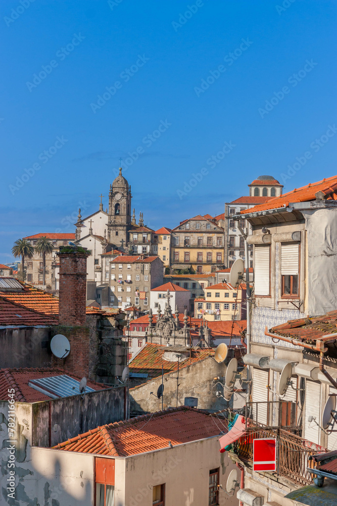 A rough and raw view of the city Porto with old ancient buildings, orange roofs and gray walls and blue sky. A vertical photo.