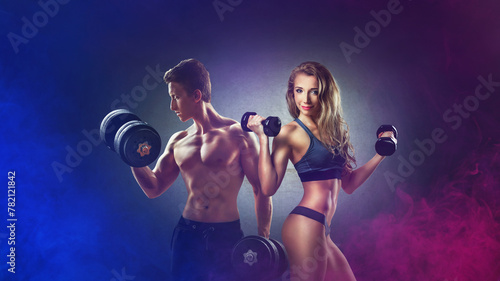 Athletic man and woman with a dumbells showing muscles. Neon light.