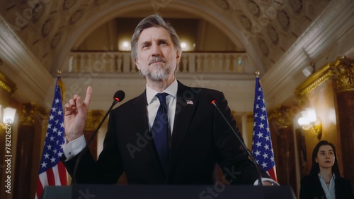 Mature US minister or politician speaks at press conference for media in White House. President of the United States gives inspirational speech, then poses for cameras. American flags in background. photo