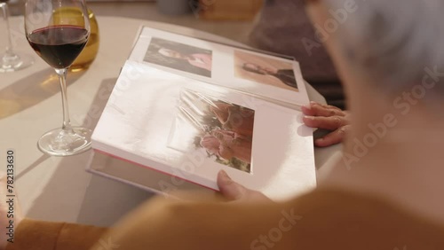 Group of diverse senior friends looking at photos in photo album and revoking memories while gathering together for dinner in apartment photo