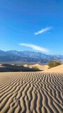 desert landscape with towering sand dunes, clear blue skies, and the distant silhouette of rugged mountains