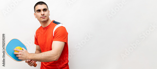 A handsome young man in his 30s is posing in sportswear and holding a pickleball racket on a white background.The man is looking to the side while having a serving pose. ©  Yistocking