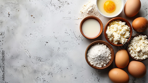 Top view of baking ingredients with eggs, flour, milk, and cottage cheese on a textured white background with copy space. photo