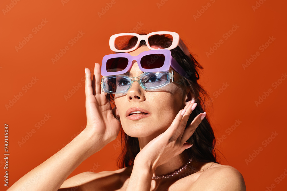 A fashionable woman strikes a pose with sunglasses perched atop her head against an orange backdrop.