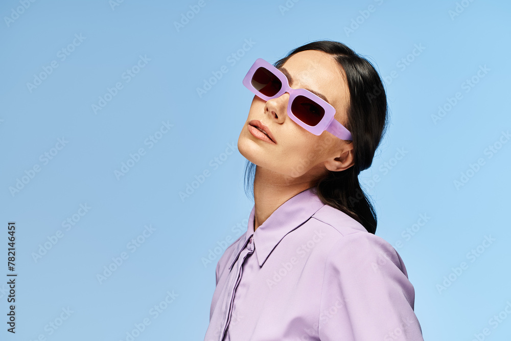 A stylish woman with purple sunglasses and shirt poses against a blue backdrop in a summery studio setting. A stylish woman with purple sunglasses and shirt poses against a blue backdrop in a summery studio setting.
