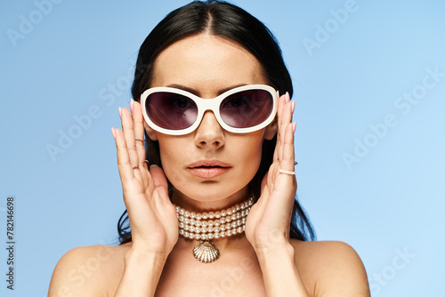 A stylish woman in sunglasses and a choker exudes confidence in a studio setting against a vibrant blue background.
