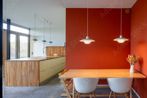 Interior of a modern home in The Netherlands. Kitchen and dining area with design lamps and an orange wall.