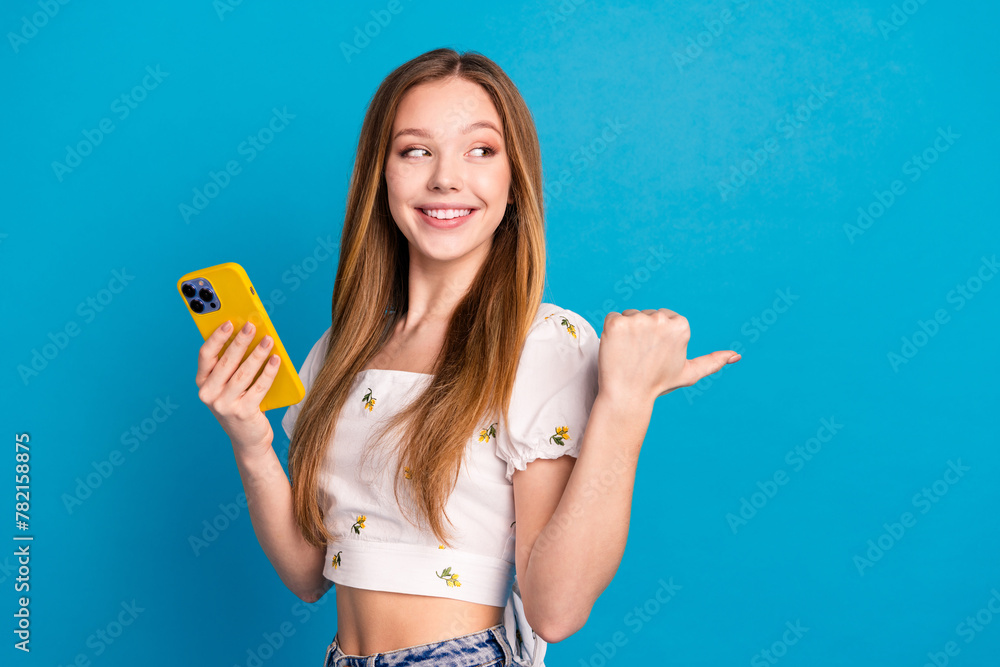 Photo of happy positive girl use cell smart gadget point finger empty space isolated blue color background Photo of happy positive girl use cell smart gadget point finger empty space isolated blue color background