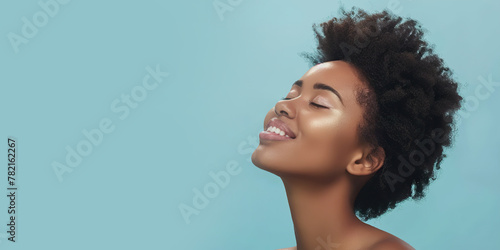 Banner portrait of serene girl with eyes closed and smile isolated on blue solid studio backdrop. Happy attractive sensual young woman with afro hairstyle, perfect skin, day makeup. Delight, enjoyment