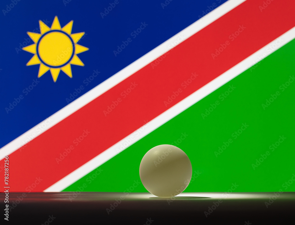 Fototapeta premium The table tennis ball stands on a surface in front of Namibia flag.