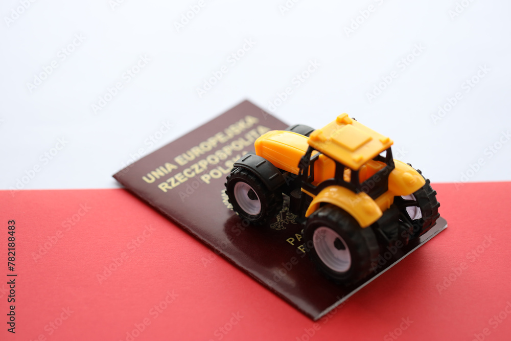 Red polish passport and yellow tractor on smooth red and white flag of Poland close up Red polish passport and yellow tractor on smooth red and white flag of Poland close up