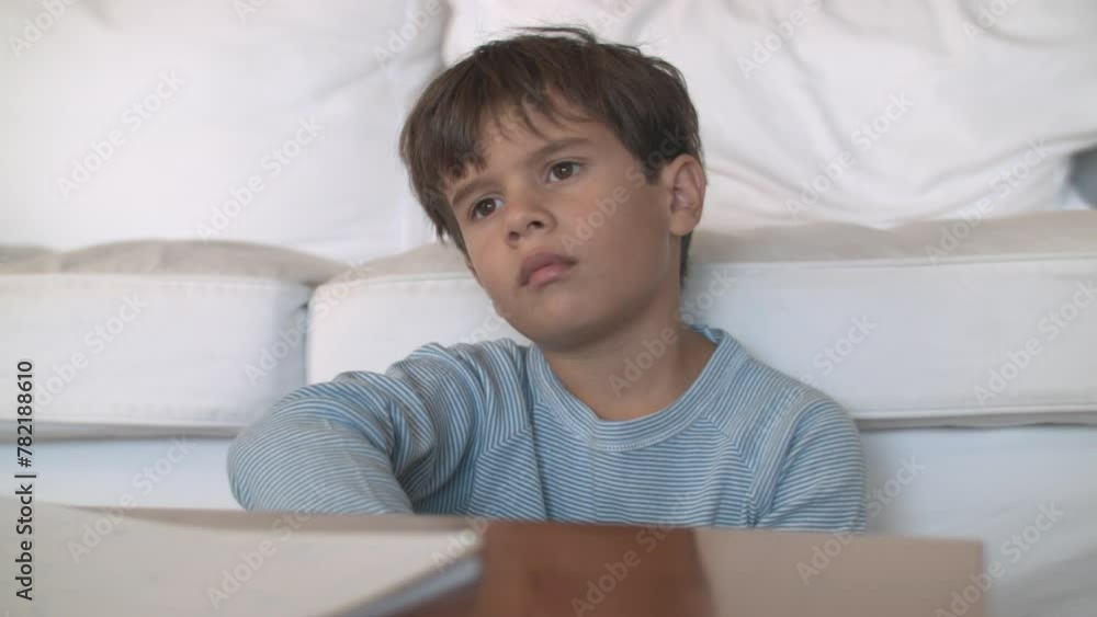 Young boy in pajamas sitting thoughtfully on a white couch Young boy in pajamas sitting thoughtfully on a white couch