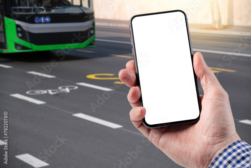 A man holds a smartphone in his hand. The bus travels along the road with markings