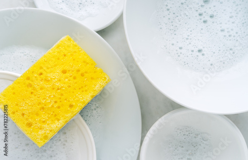 Yellow sponge and a soapy foam, white plate with soap suds on a background. Cleaning concept, cleaning service, flat lay, top view